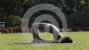 Video of a woman practicing shoulder-supported bridge, also known as bridge exercise, in a park.Â 